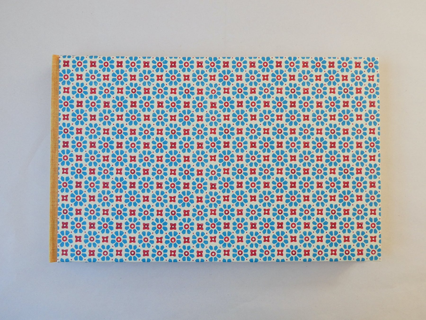 Handmade sketchbook with blue and red Italian patterned paper cover on a white background