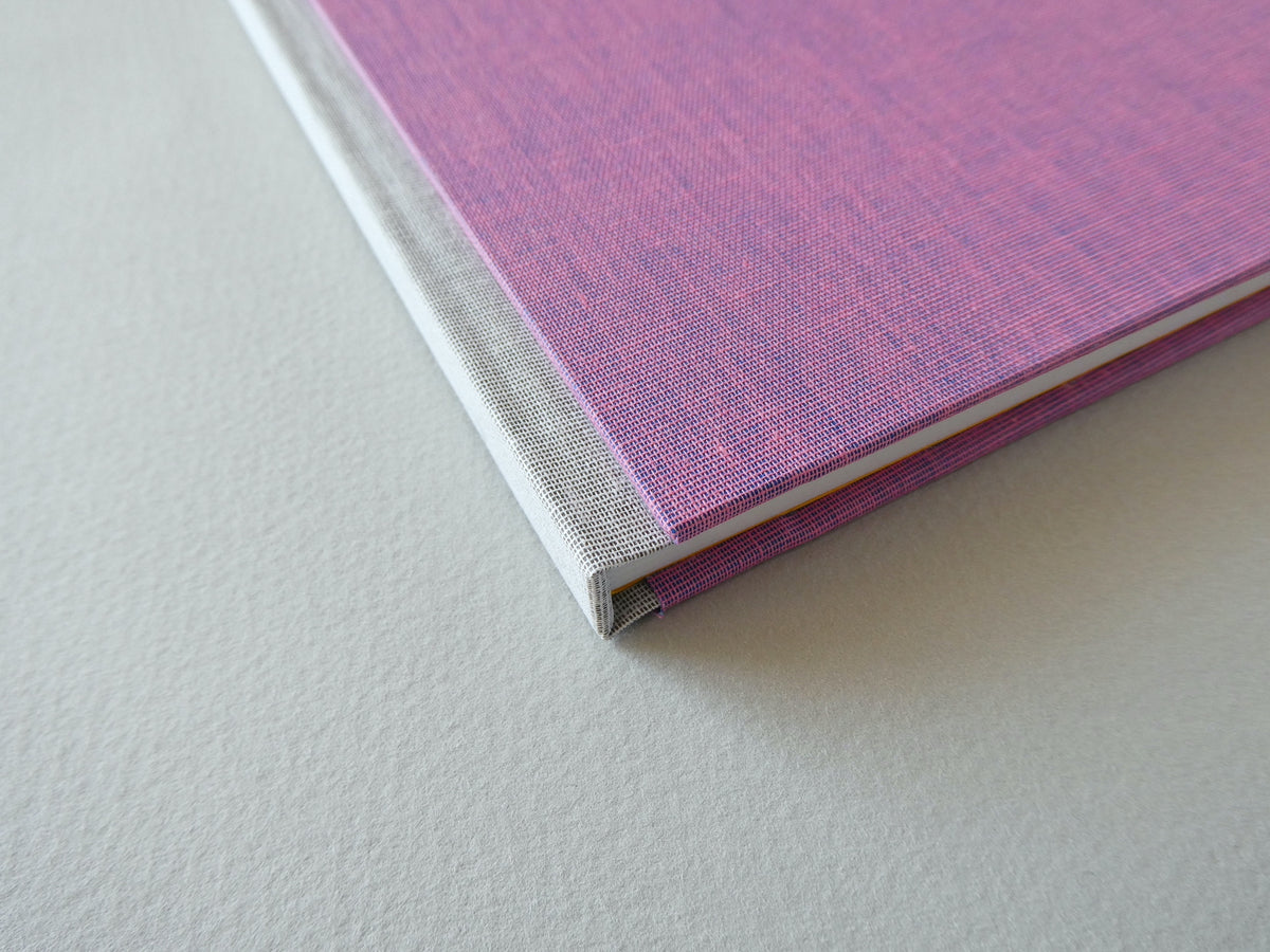 Close-up of a pink hand bound sketchbook on a light grey surface