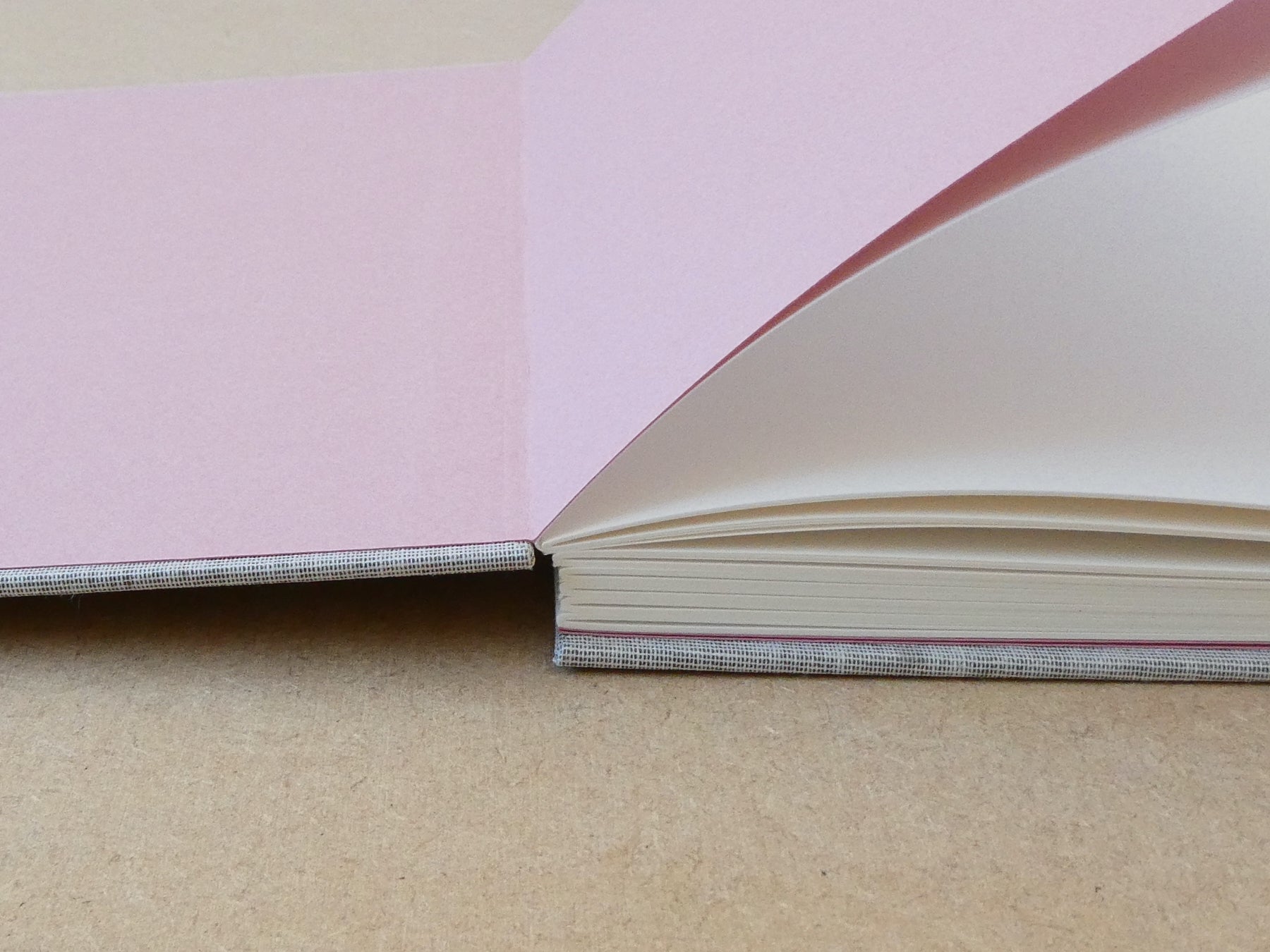 Close-up of a book with pink endpapers and a grey cover on a light brown surface.