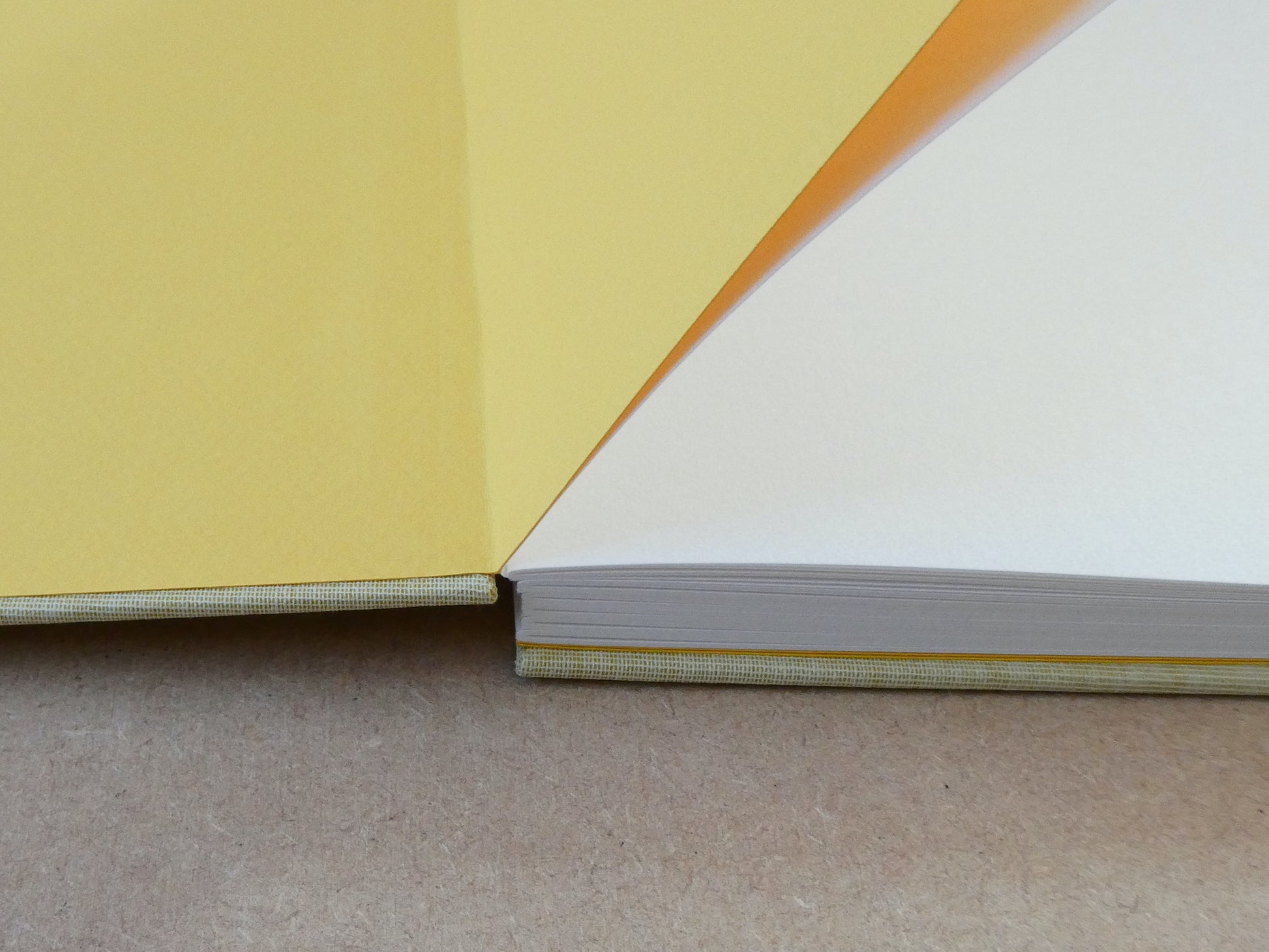 Close up of a handmade book with ellow endpapers and white paper on a brown surface
