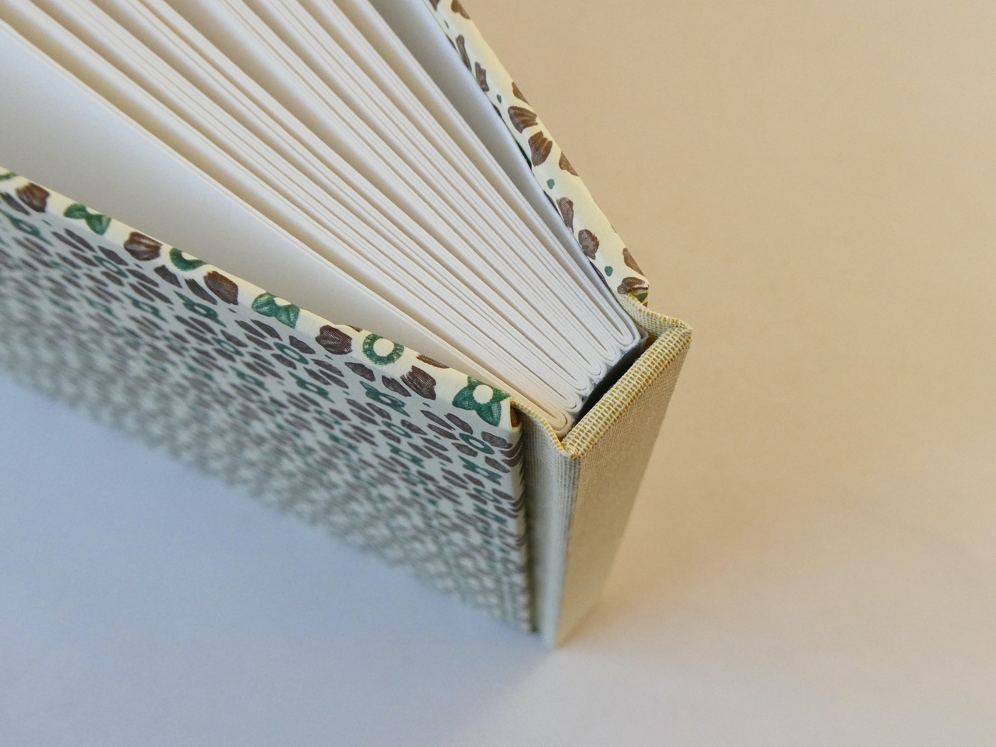 Close-up of a handmade sketchbook with patterned cover and white pages on a gradient background