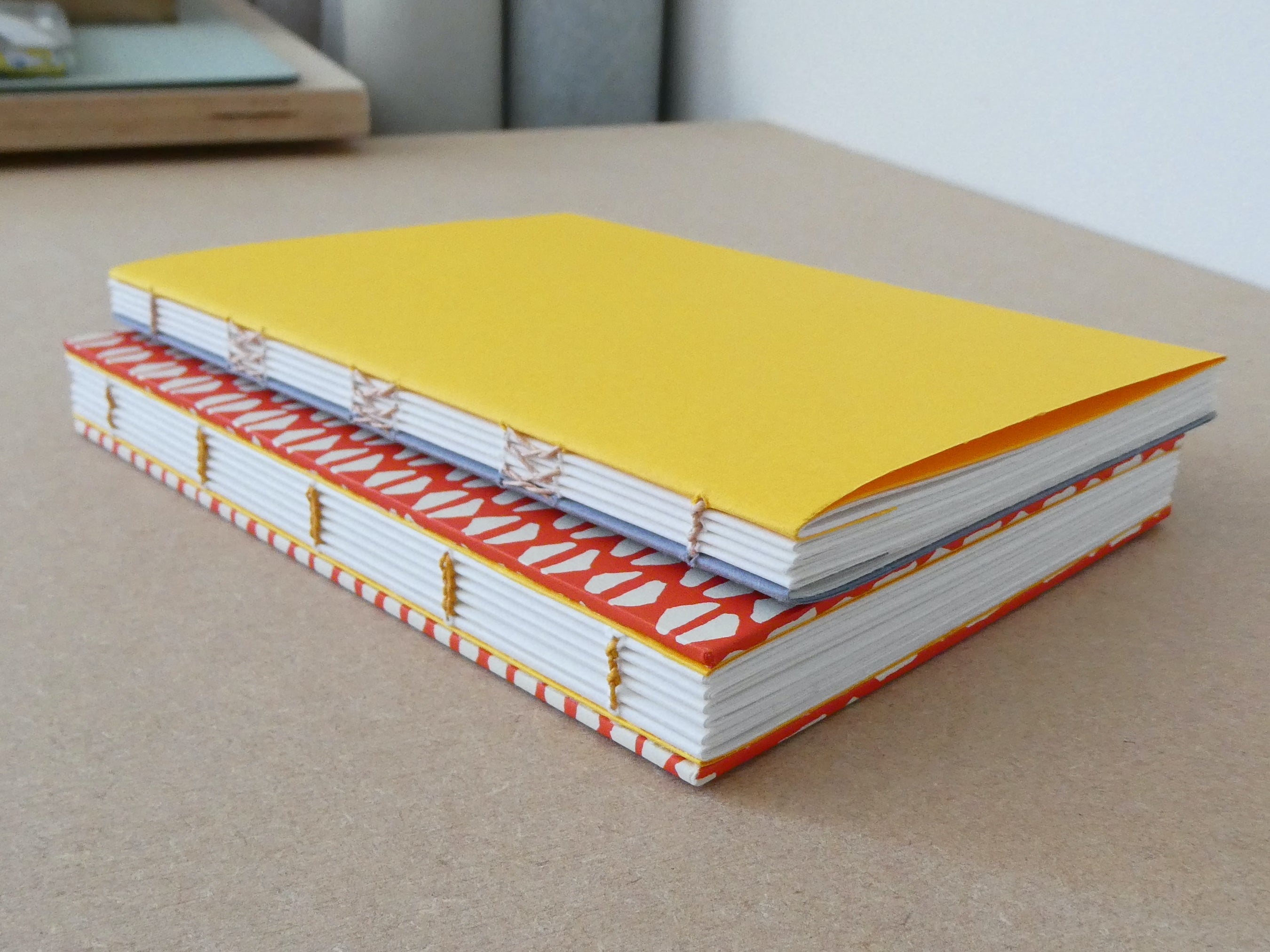 Two notebooks with yellow, white, and red covers on a beige surface.