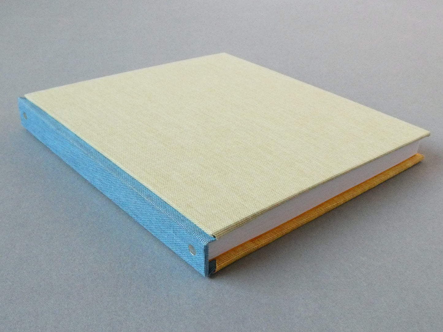 Hand bound sketchbook with a blue spine and beige cover on a gray background