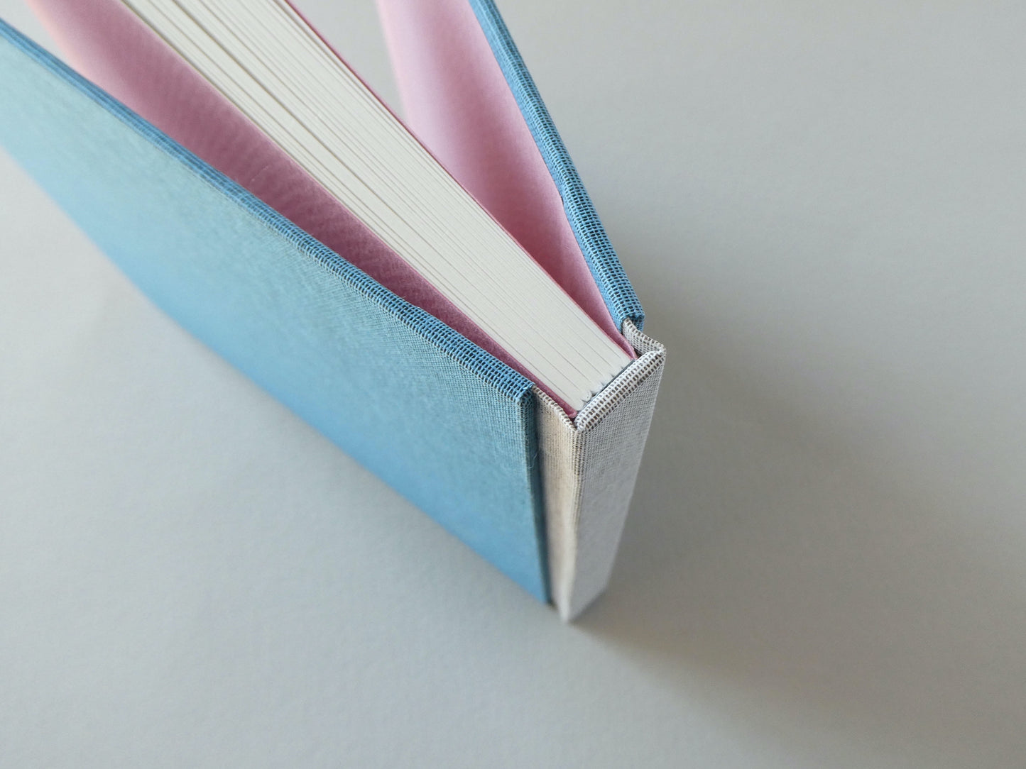 Close-up of a blue handbound book with pink endpapers on a light grey background