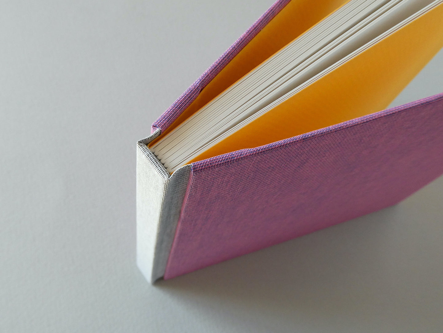 Close-up of a pink hand bound sketchbook with yellow endpapers on a grey background